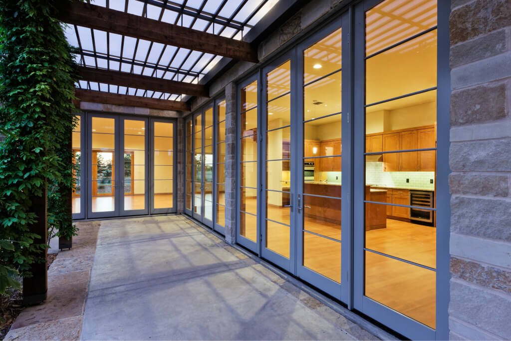 Row of black-framed glass doors along a covered patio, with a lit kitchen inside