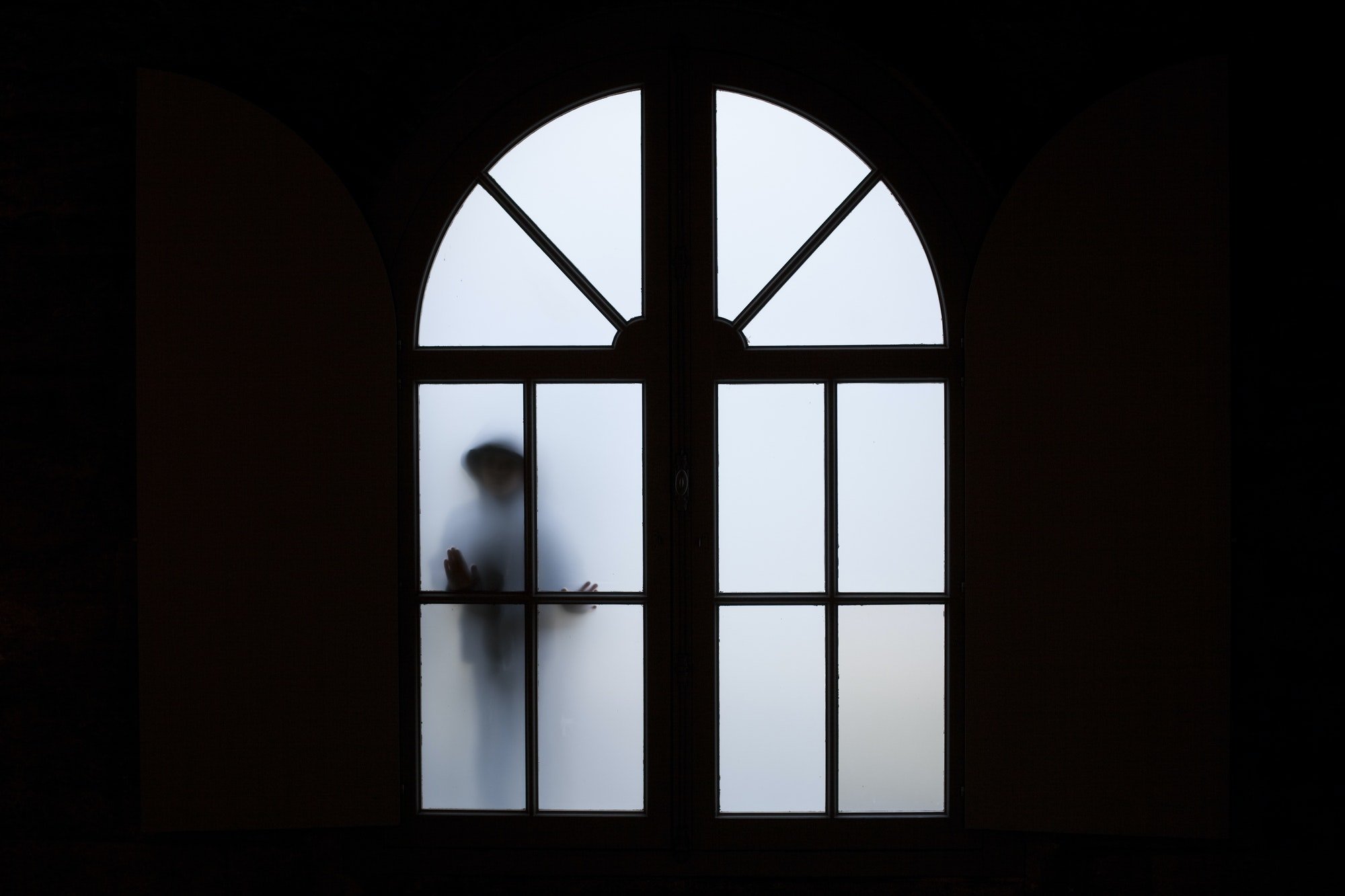 Silhouette of a person behind a frosted arched window in a dark room